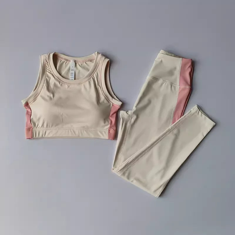 A two-piece activewear set consisting of a beige sports bra with pink side panels and matching high-waisted leggings with pink side panels, laid flat on a light gray background.