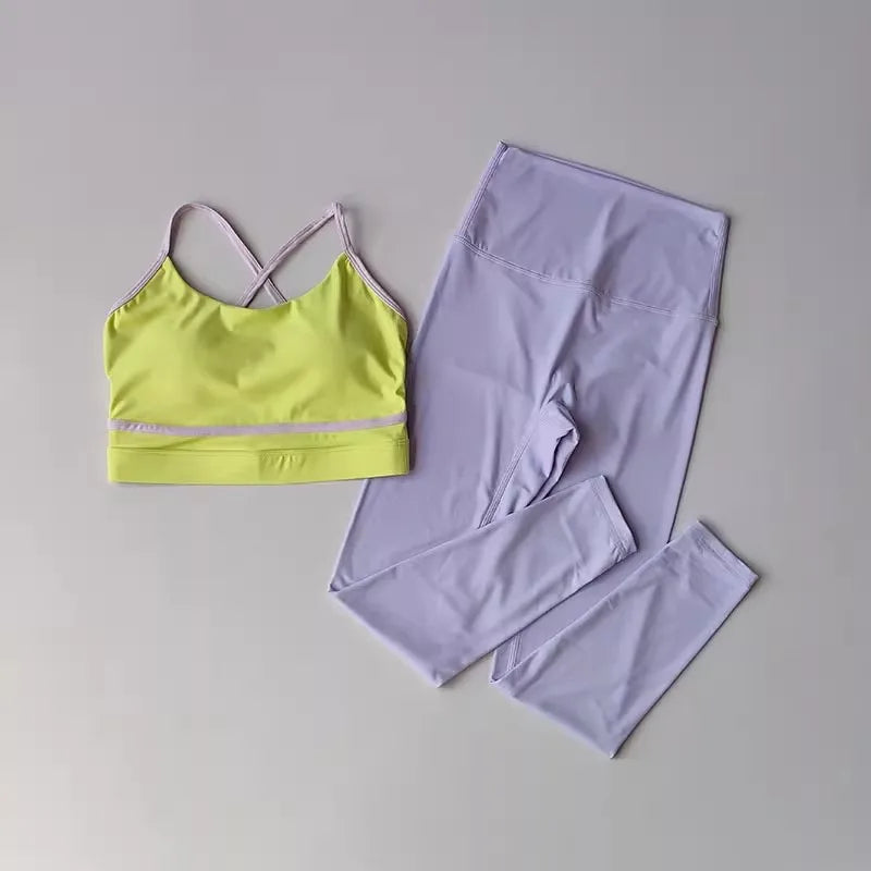 A two-piece activewear set laid flat on a light gray background, featuring a lime green sports bra with light purple straps and trim, paired with high-waisted light purple leggings.