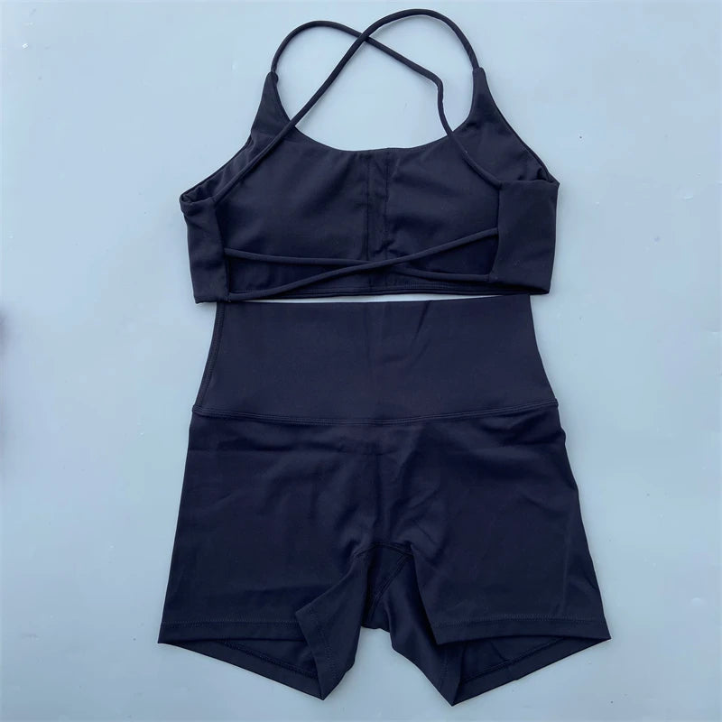 A two-piece athletic set consisting of a dark navy sports bra with crossover straps and matching high-waisted shorts, laid flat on a light blue-gray background.