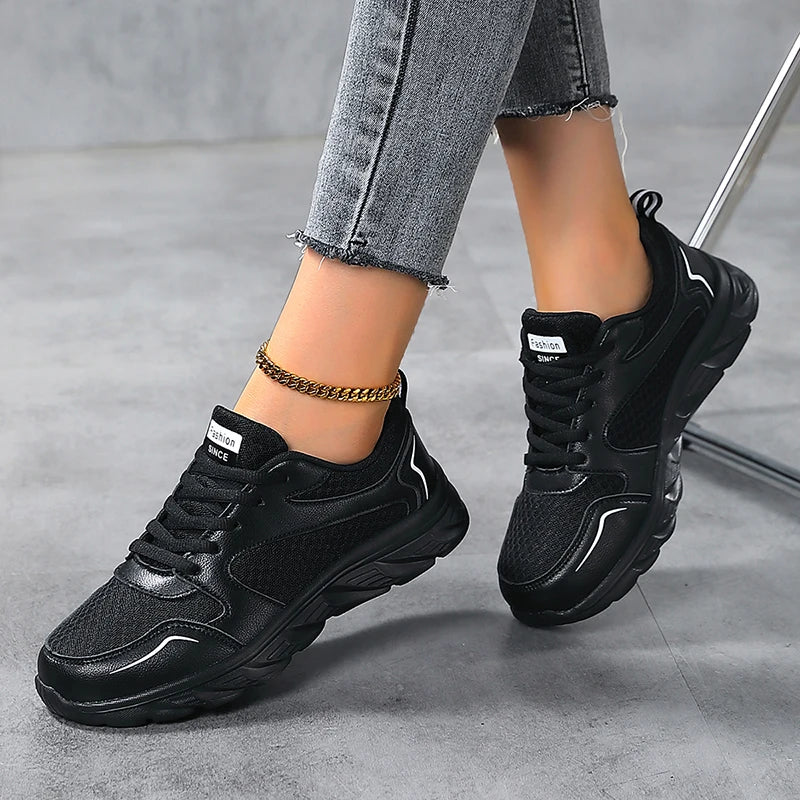 Black sneakers worn with gray jeans on a gray floor.