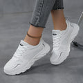 White sneakers worn with gray jeans on a gray floor.