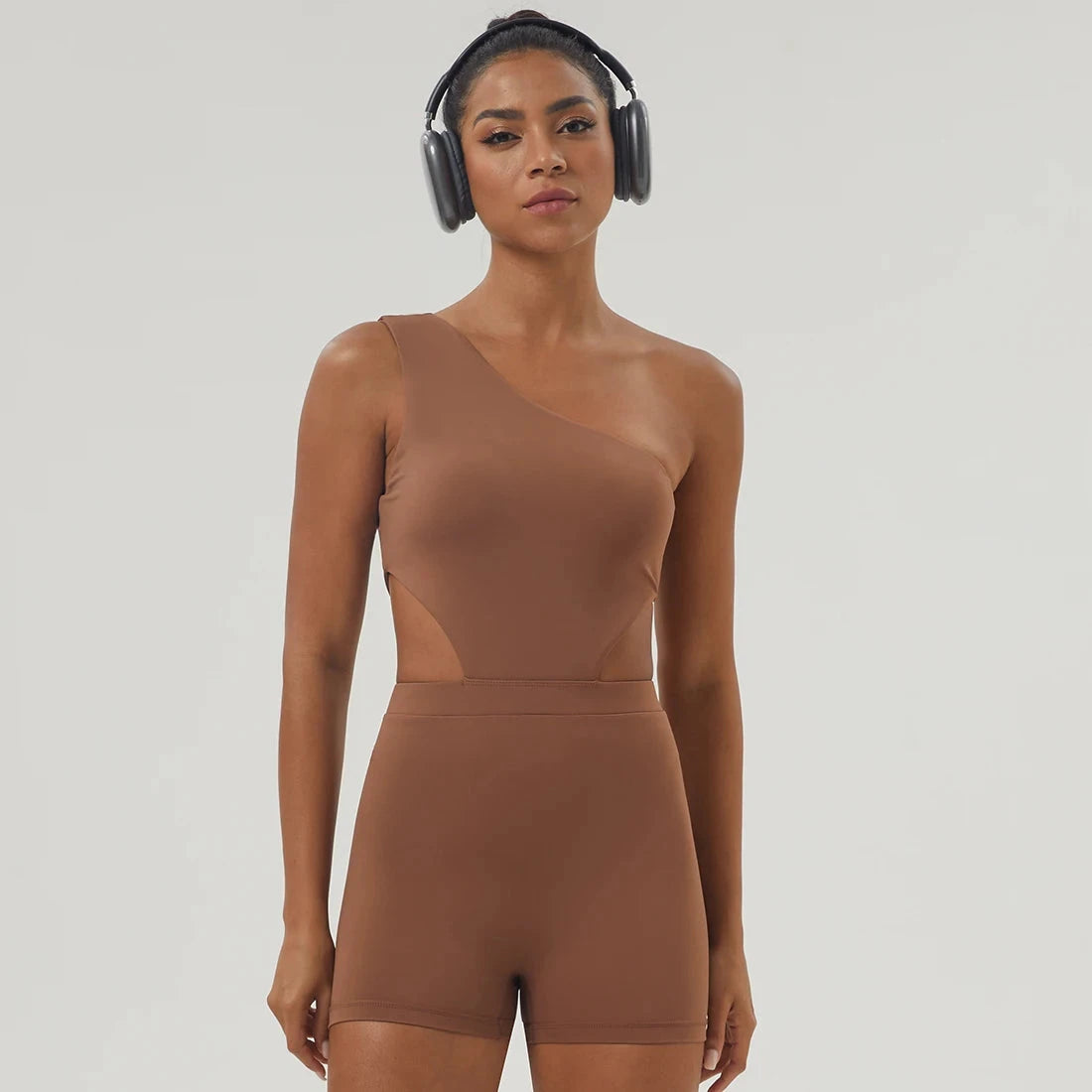 Brown Women One-Shoulder Sport Bodyduit Jumpsuit with headphones, featuring padded bust and cutout sides for stylish workouts.